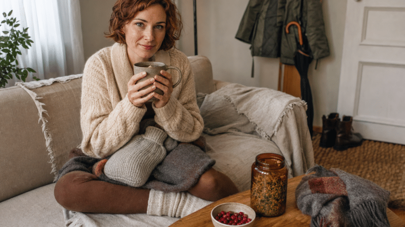 felfázás megelőzése: nő meleg pulóverben, tea és tőzegáfonya